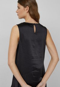 Zwarte mouwloze top met een gladde, glanzende textuur, voorzien van een keyhole detail aan de achterkant en een asymmetrisch zoomontwerp.