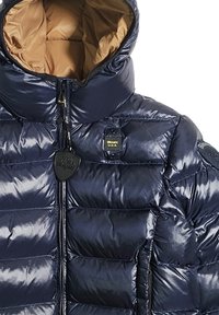 Giacca a vento blu navy con un esterno lucido e trapuntato, colletto alto e fodera beige a contrasto, dotata di zip frontale e etichette di marca.