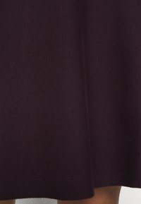 Tissu tricoté violet foncé drapé sur le genou d'une personne, montrant un tricot finement texturé et un détail de couture verticale.