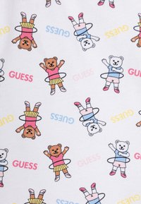 Tessuto bianco con personaggi orso colorati in outfit rosa e blu, che tengono hula hoop, e la parola "GUESS" in vari colori.