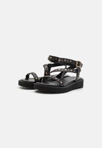 Sorte sandaler med flere remmer som har gullnitter og spenne. Tykk, teksturert såle med et lett platådesign.