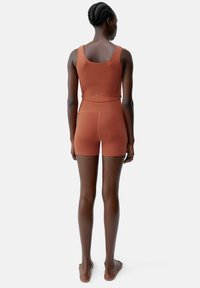 Rustfärgad träningsuppsättning med en åtsittande crop top och shorts. Tillverkad av stretchigt material med en slät yta och minimala sömmar.