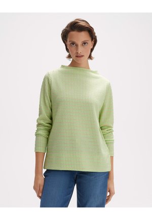 Grüner strukturierter Pullover mit boxy Form, langen Ärmeln und hohem Kragen. Verfügt über ein dezentes Karomuster. Kombination mit blauen Jeans.