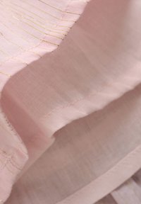 Ljusrosa tyg med fina gyllene ränder. Mjuk textur, något skrynklig med synlig sömnad längs kanterna. Lätt material.