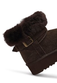 Braune Wildleder-Stiefelette mit einem strukturierten, braunen Kunstfellbund, ausgestattet mit einer goldenen Metallschnalle und einer robusten Sohle mit Rillen.