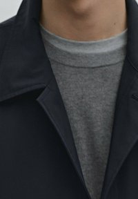 Marineblauer Blazer mit breitem Kragen über einem hellgrauen Rundhals-T-Shirt. Die Stoffe wirken glatt und weich, mit einem sauberen, modernen Design.