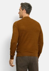 Brauner Strickpullover mit gerippten Bündchen und Saum, der eine subtile Textur aufweist. Trägt dunkle graue Hosen und zeigt eine Rückansicht.