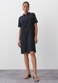 Schwarzes Leinenhemdkleid mit kurzen Ärmeln, Kragen und zwei vorderen Taschen. Verfügt über eine Knopfleiste und einen leicht lockeren Schnitt.