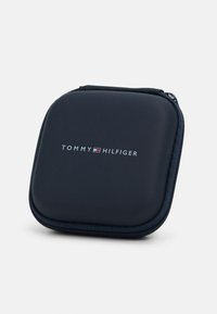 Tumed sinine kõvakaaneline kott sileda tekstuuriga, millel on valge "TOMMY HILFIGER" logo. Kindel lukustus ja ümarad servad.