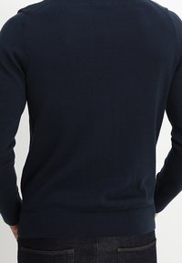 Granatowy dzianinowy sweter z długimi rękawami, ściągaczami na mankietach i dole, charakteryzujący się gładką fakturą i dopasowanym krojem.