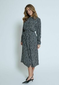 Randig klänning i svart och vitt med krage, lång ärm, smal midja och knälång nederkant. Bärs med svarta slingbacks.