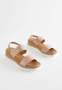 Blush pink wedge sandals with two wide straps, textured wood heel, white rubber sole, and buckle closure.
