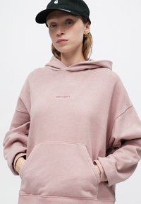 Túlméretezett rózsaszín kapucnis pulóver, elülső zsebbel és hímzett logóval. Puha anyag és bordás mandzsetta egészíti ki a dizájnt.