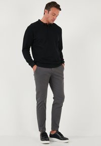 Polo de manga larga negro, textura acanalada, combinado con pantalones ajustados grises y zapatillas negras con suelas blancas. Look casual.