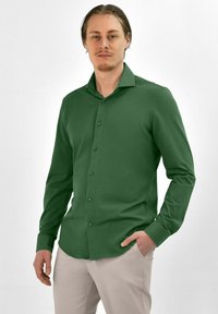 Groene lange mouwen shirt met een button-down kraag, zachte textuur en bijpassende knopen, gedragen met lichtgekleurde broeken.