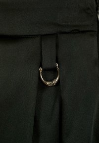 Tessuto nero con una superficie liscia, caratterizzato da una piega e un dettaglio in acciaio inox argentato con una incisione della lettera "R".