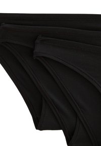 Des culottes noires en coton exposées dans un arrangement empilé, avec de fines ceintures élastiques, une texture lisse et des détails de couture subtils.