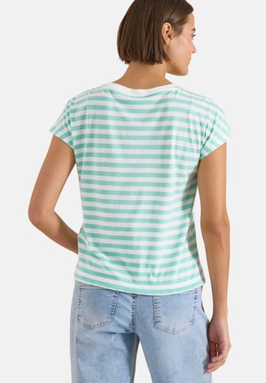 Femme aux cheveux courts et bruns portant un t-shirt à manches courtes rayé vert menthe et blanc et un jean en denim bleu clair, vue de dos.