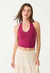 Magenta halter crop top yang terbuat dari bahan elastis dengan leher V yang dalam. Dipadukan dengan rok maxi berlapis beige muda yang memiliki waistband elastis.