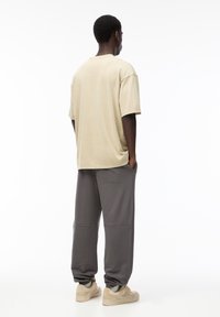Beige bomulds t-shirt med korte ærmer, parret med grå sweatpants med sidelommer og elastiske manchetter. Lyse sko fuldender looket.