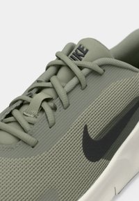 Baskets en maille verte avec semelle en caoutchouc, dotées de lacets ton sur ton et d'un logo Nike swoosh noir sur le côté. Tige texturée avec des rayures subtiles.