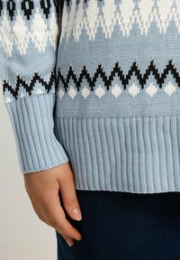 Maglione lavorato a maglia azzurro chiaro con un motivo a diamanti bianchi e neri. Presenta polsini e orlo a costine, tessuto texturizzato.