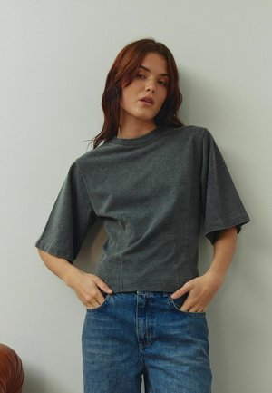 Pelēka īsroku krekls no mīksta auduma ar vaļēju piegriezumu, ar augstu apkakli un sānu šuvēm. Saskaņots ar gaismazilas krāsas džinsa biksēm.