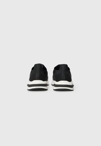 Pantofi sport negri cu un superior din tricot, guler rotunjit și talpă albă cu dungi negre. Design minimalist fără logo-uri vizibile.