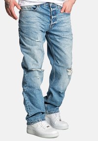 Hellblaue, ausgebleichte Jeans im distressed Look mit lockerer Passform, die Risse an den Knien und einen umgeschlagenen Saum aufweisen, kombiniert mit weißen Sneakers.