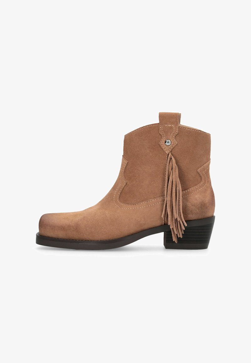 Bottine en daim marron avec un petit talon carré, bords festonnés et un accent décoratif à pompon. Texture lisse, design à bout arrondi.