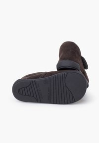 Pantof maro din piele întoarsă cu talpă texturată din cauciuc. Are un vârf rotund și o curea cu Velcro. Partea de jos a tălpii are un model antiderapant pentru aderență.