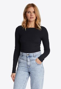 Zwarte ribbeltop met lange mouwen gecombineerd met lichtblauwe denim jeans met hoge taille, voorzien van opgestikte zakken en een knoopsluiting.