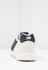 Tenisky New Balance v námořnické semišové a bílé síťovině, s texturovaným patkem a detailem loga. Zakřivená podrážka s gumovým vzorkem.