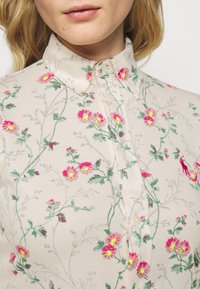 Blumiges Hemd mit Knöpfen in Cremefarbe, gestickten pinken und gelben Blumen, und einem klassischen Kragen mit weißen Knopfverschlüssen.