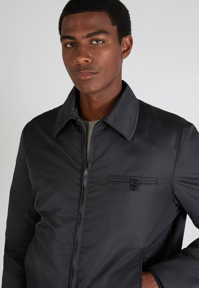 Giacca nera con zip, tasca con bottone a pressione, colletto e tessuto liscio e lucido. Caratterizzata da un design slanciato con una silhouette aderente.