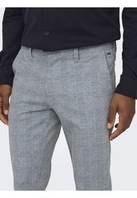 Pantalones de cuadros grises con una tela texturizada, presentan un frente plano y bolsillos laterales. Combinados con una camisa de botones oscura.