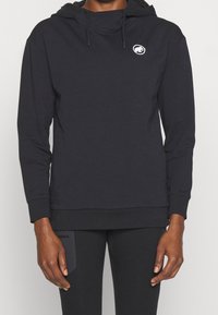 Sudadera negra hecha de una tela suave, con bolsillo tipo canguro, dobladillo ajustado y un logo bordado en el pecho. Mangas largas, corte relajado.