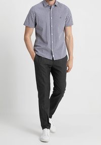 Camicia a maniche corte a scacchi blu e bianchi con bottoni, abbinata a pantaloni scuri in tessuto e sneaker bianche.