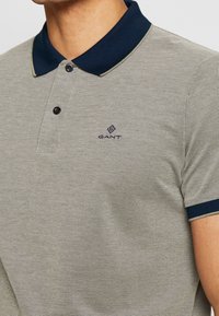 Koszulka polo z krótkim rękawem wykonana z teksturowanej szarej tkaniny, z granatowym kołnierzykiem i wykończeniem rękawów oraz małym haftowanym logo na piersi.