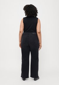 Black wide-leg jeans with a high waist, featuring back pockets and a belt loop. The fabric has a smooth texture. Worn with a sleeveless top.