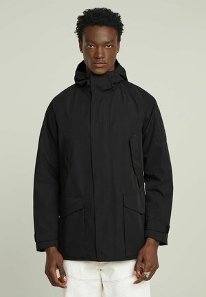 Veste imperméable noire avec un col haut, des poches avant et des poignets ajustables ; dispose d'une capuche pour une protection supplémentaire contre les intempéries.