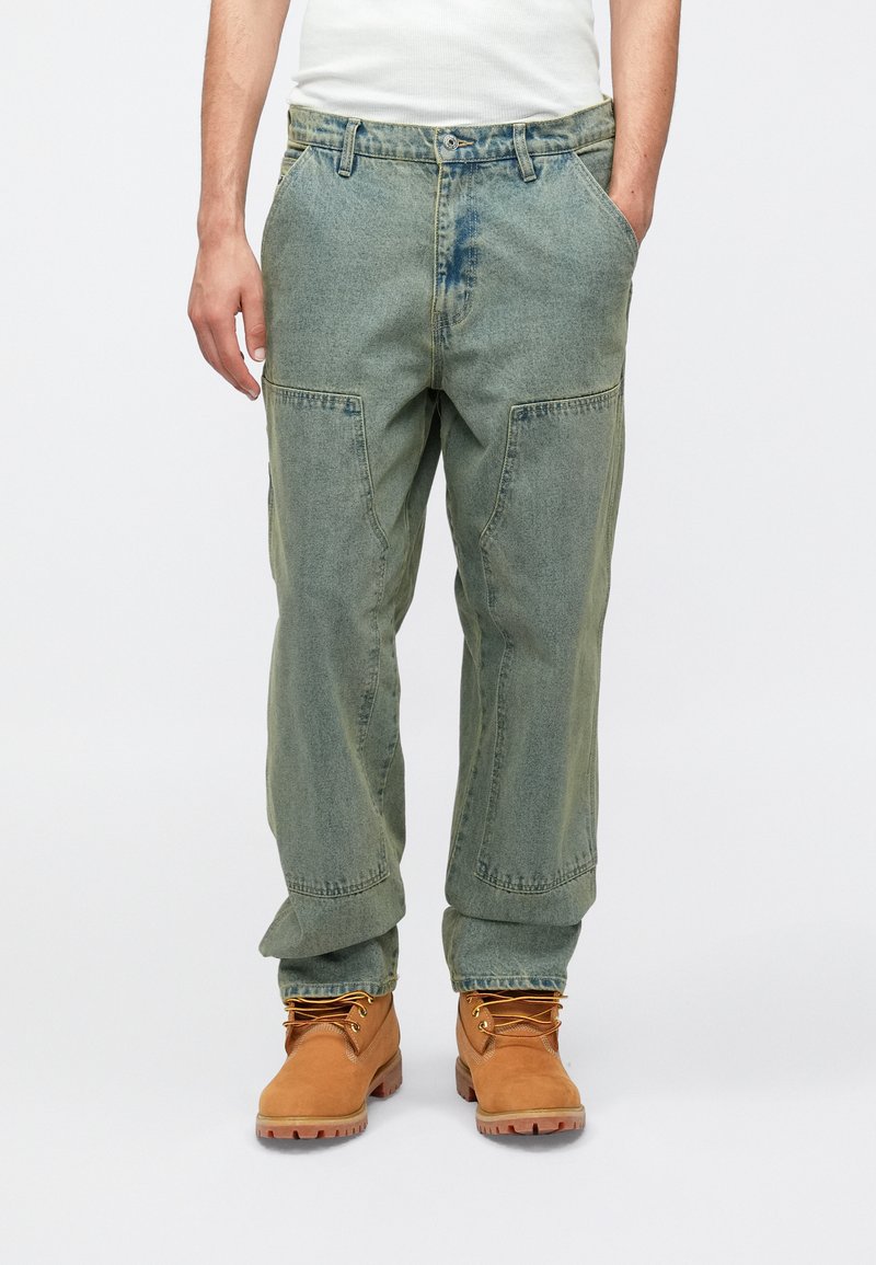 Πράσινο τζιν cargo παντελόνι με άνετη εφαρμογή, πολλαπλές πλαϊνές τσέπες και ευθεία γραμμή στο πόδι· συνδυασμένο με ταμπά εργοταξιακά μποτάκια με κορδόνια.