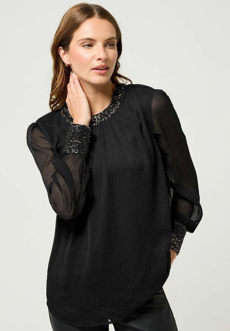 Blusa nera realizzata in tessuto trasparente con un design plissettato. Presenta un colletto e polsini decorati con perline, maniche lunghe e una vestibilità comoda.