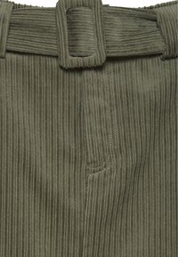 Olivgrön manchester med vertikala ribbor, med ett bälte, sydda fickdetaljer och en mjuk textur.