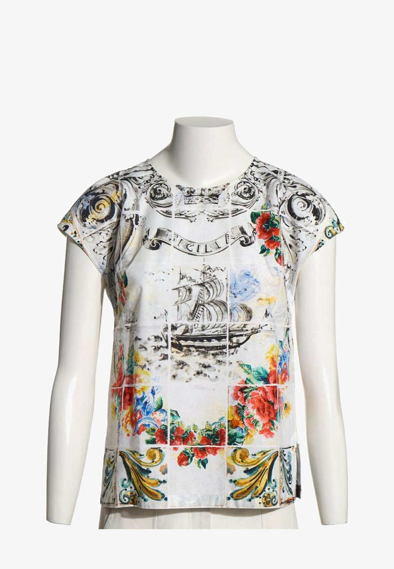 Chemise blanche à manches courtes avec des motifs floraux colorés, un voilier et des volutes décoratives sur un mannequin buste.