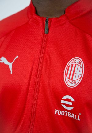 Giacca rossa Puma con zip, caratterizzata da un tessuto testurizzato, zip frontale, logo AC Milan e dettagli di branding bianchi sul lato sinistro del petto.