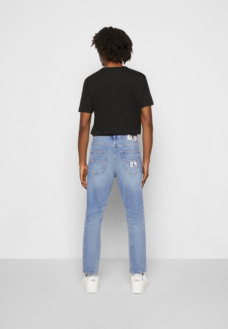 Svart t-shirt med kort ärm i kombination med ljusblå denimjeans, med bakfickor och en synlig logotyp på midjebandet.