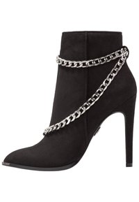 Bottine en daim noir avec bout pointu, talon stiletto haut et accent de chaîne argentée autour de la cheville. Texture lisse, design élégant.