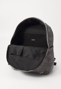 Gray fabric backpack with a large opening, featuring a black interior, zip closure, and a label reading "YOURTURN." Includes inner pocket.