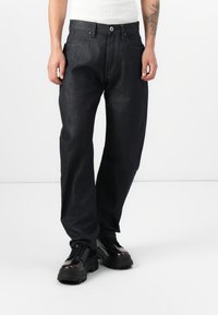 Dark denim jeans with a straight fit, front pockets, and a button fly closure. Worn with black chunky-soled shoes. Smooth texture.